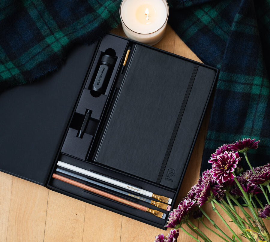 A Blackwing Notebook Essentials Set, Blackwing pencils, and a candle on a wooden table.