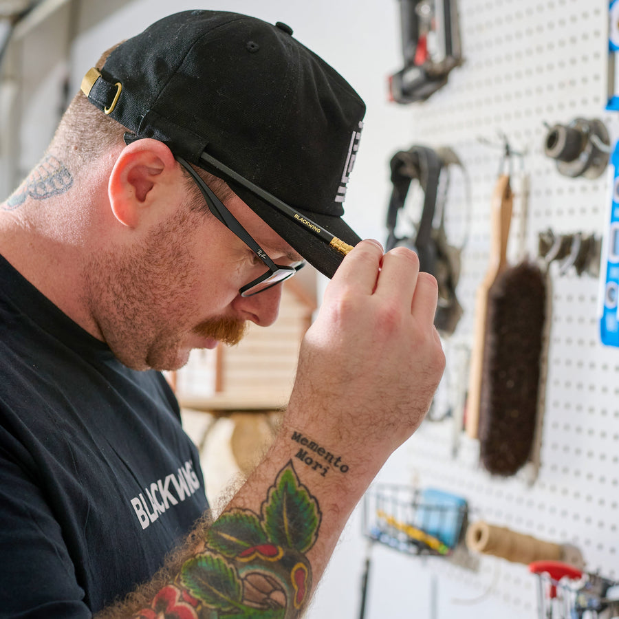 man in his shop wearing a Blackwing canvas cap with a Blackwing Matte pencil looped into the side loop of the hat