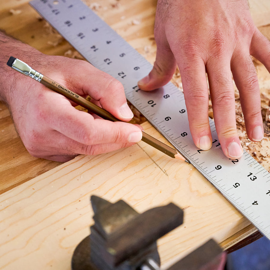Person measuring wood with a ruler and marking with a Blackwing pencil for woodwork