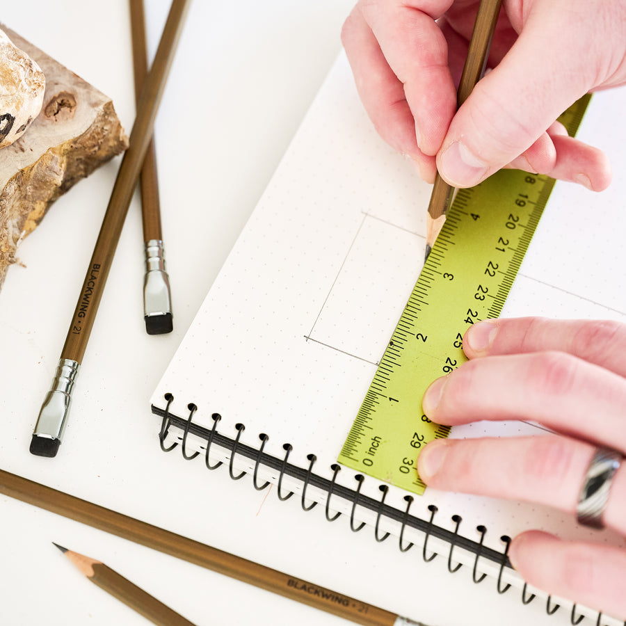 Person using a ruler and Blackwing Volume 21 woodworking pencil on a notebook 