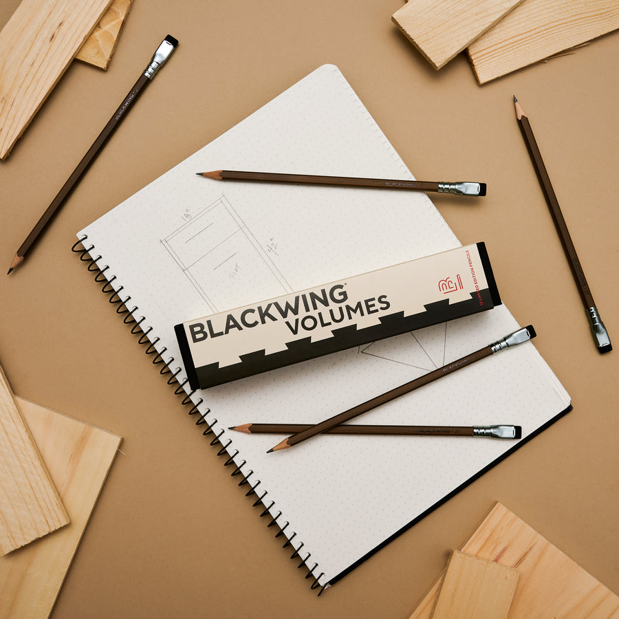 Blackwing Volume 21 pencils scattered on a surface with a notebook and wood