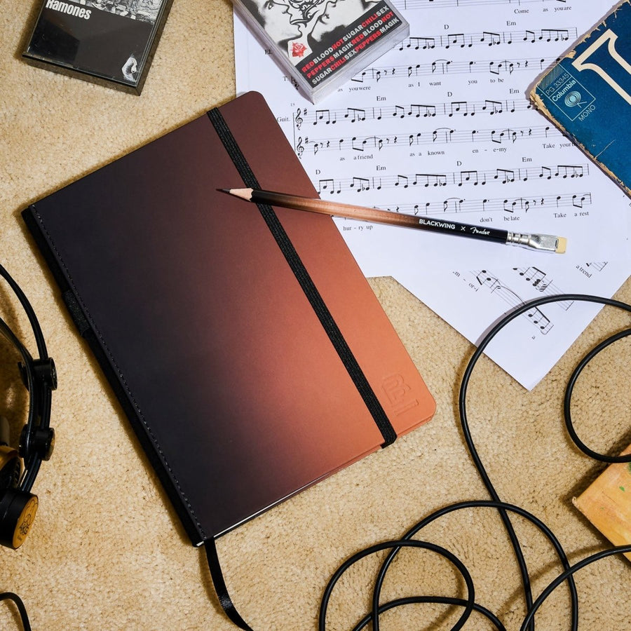 Blackwing x Fender notebook and pencil layng next to aux cord and music sheets
