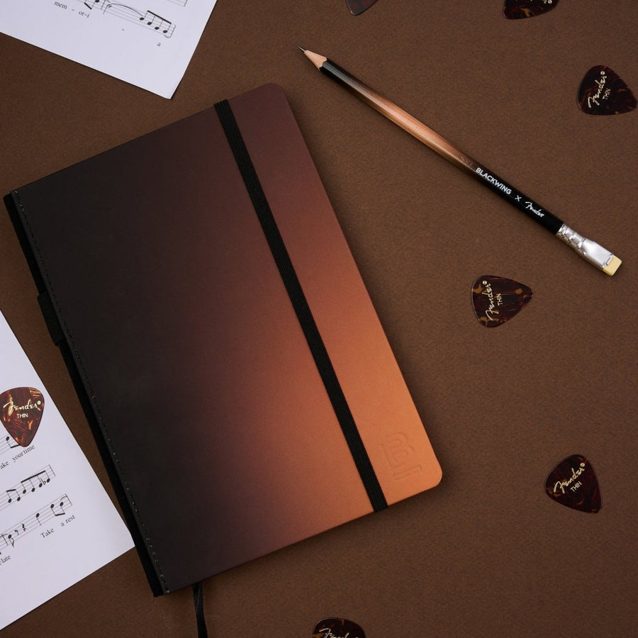Blackwing x Fender notebook and pencil laying on a table with music sheets and guitar picks