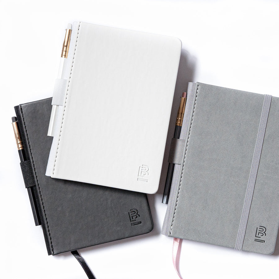 Three notebooks, one with a Small Blackwing Slate Notebook - White, pens, and pencils on a white surface.